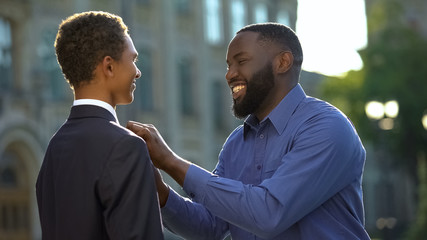 Excited african man feeling proud of young son in prom suit, college graduation © motortion