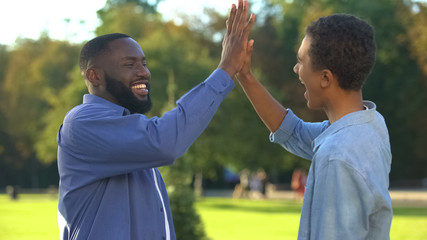 Cheerful black brothers giving high five outdoors, happy family, close relations