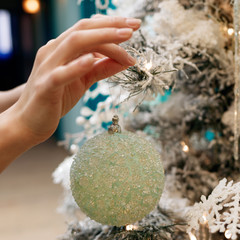 Hands decorating christmas tree with a silver balls.