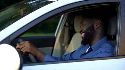 Fototapeta na wymiar Cheerful adult afro-american man driving new auto, enjoying trip and smiling
