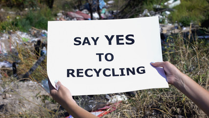 Say yes to recycling phrase on cardboard in hands against landfill background
