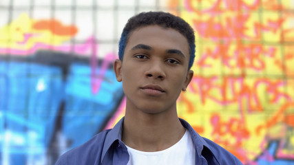 Cool male teenager with colored hair looking camera on graffiti wall background