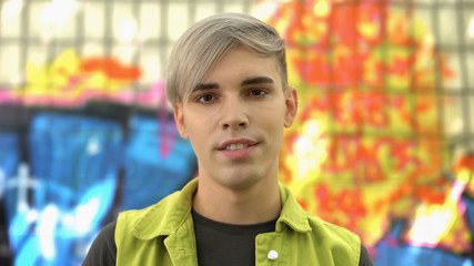 Pierced young man looking camera standing graffiti wall background, urban style