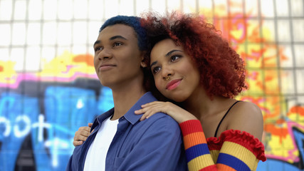 Red-haired female teenager hugging boyfriend graffiti wall background, culture