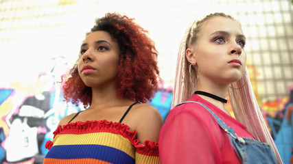 Two confident female teenagers standing back to back, new generation trends