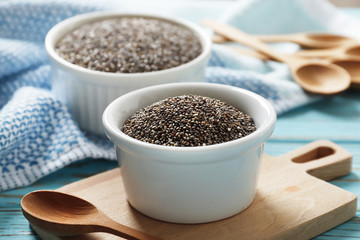 Bowl and spoons with chia on blue wooden background, close up