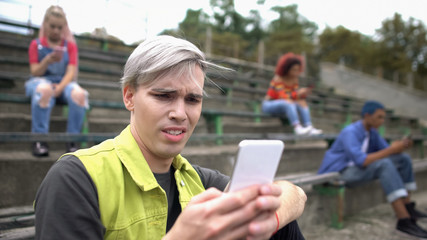 Male teenager watching unpleasant photo online, scrolling social network app