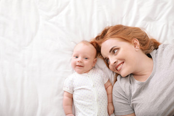 Mother with cute baby lying on bed, top view