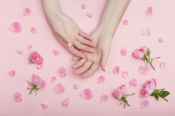 Obraz na płótnie Canvas Beauty Hand of a woman with red flowers lies on table, pink paper background. Natural cosmetics product and hand care, moisturizing and wrinkle reduction, skincare
