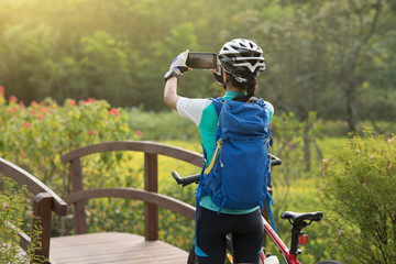 Woman using smartphone taking photo while riding bike on sunny day in park