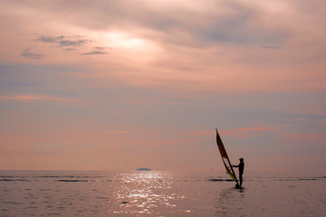 A woman sailing on a windsurfing board while on the sea in the evening.