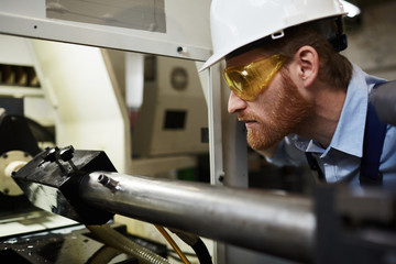 Close-up of technician in work helmet and in protective glasses examining the work of new lathe in the plant