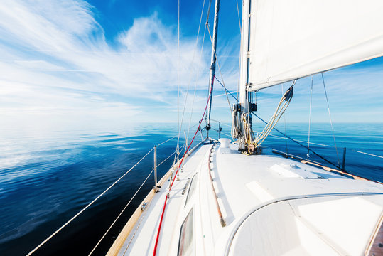 White sloop rigged yacht sailing in an open Baltic sea on a clear sunny day. A view from the deck to the bow, mast and sails. Estonia