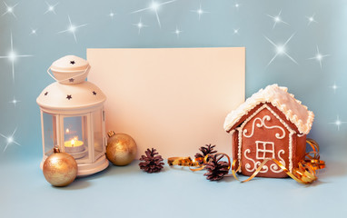 White lantern, little gingerbread house with glaze, empty card for your text and christmas balls on blue background. Holiday mood.