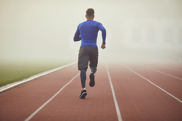 Training in the fog. A young athlete runs on a stadium in the fog