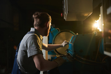 Manual worker in work wear working at the lathe at manufacturing fabric