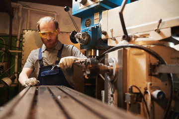 Young worker in protective glasses working on lathe in the factory