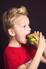 funny boy close-up with open mouth eats a delicious burger with chicken, vegetables and cheese
