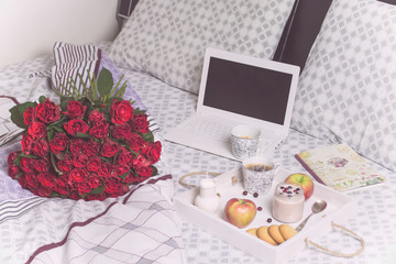 beautiful bouquet of red roses and breakfast with coffee, fruit smoothie in bed near a laptop