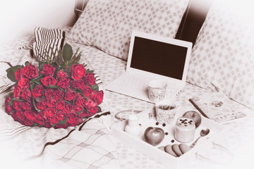 beautiful bouquet of red roses and breakfast with coffee, fruit smoothie in bed near a laptop