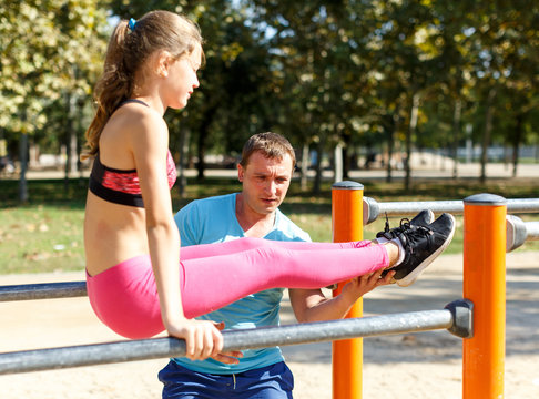 Girl with father doing l-sit on parallel bars