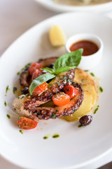 Grilled Octopus with Roasted Vegetables and Olives on White Plate.