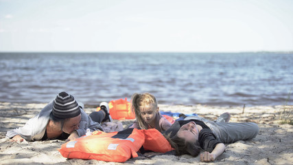 Women and child lying on shore after shipwreck, refugee survivors