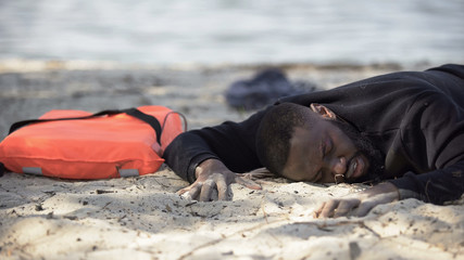 African-american man lying on shore suffering pain, refugee survived shipwreck