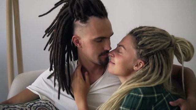 Portrait of a beautiful couple with dreadlocks - husband and wife in their new apartment. The guy and the girl embrace and kiss, their faces are close to each other. Adorable relationships. Close up