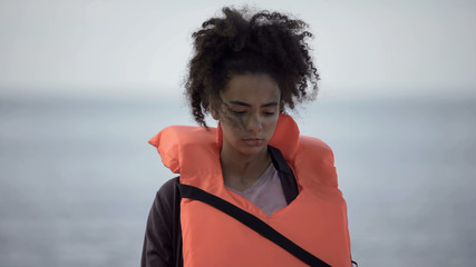 Sad teenage girl in life jacket looking distressed and lonely, disaster victim