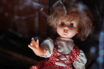 Old doll with scary look in red dress with spider web in front of her. Halloween