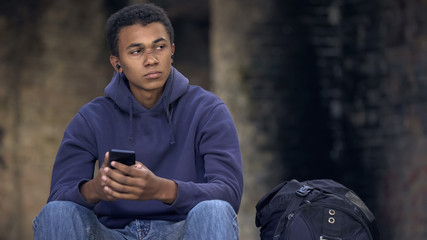Lonely young man listening smartphone music sitting street, puberty insecurities