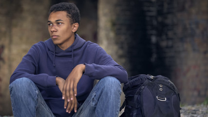 Lonely afro-american teenager sitting in abandoned house and waiting for friends