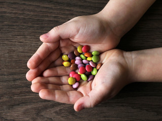 Colored candy drops in children's hands, top view