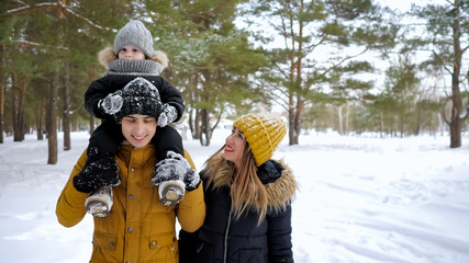 Happy young family, mom, son and dad are walking together in winter park.
