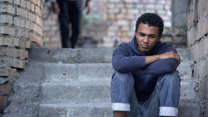 Fototapeta na wymiar Pensive afro-american teenager sitting on stairs, misunderstanding with parents