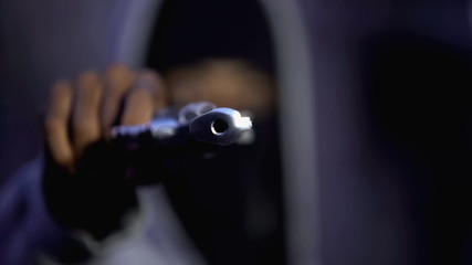 Black criminal in balaclava aiming gun camera, threatening burglar at victim