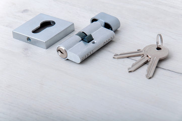Lock core and door keys on a light background. Repair in the house. Installing a new lock on the door. Spare parts for the door on a gray wooden table.