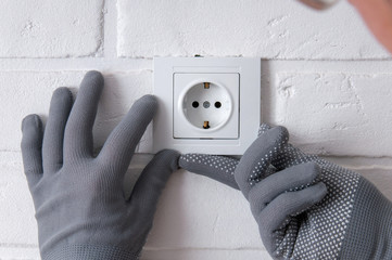 The guy installs new sockets. Repair in the house. The guy twists the screws on the sockets with a screwdriver. Rosette on a white loft background.