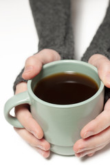 Holding green cup with tea, coffee in hands wearing mitts