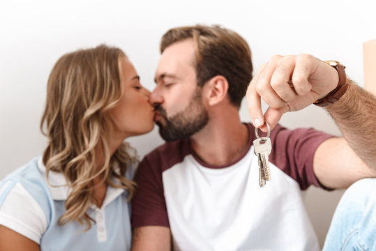 Photo of romantic couple holding keys and kissing while sitting on floor