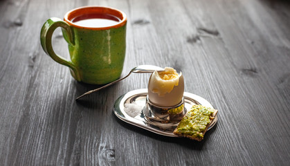 Breakfast on wooden table. Boiled egg in a stand, bread with avocado and a cup of tea