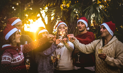 Friends group with santa hats celebrating Christmas with champagne wine toast outdoors - Tropical...
