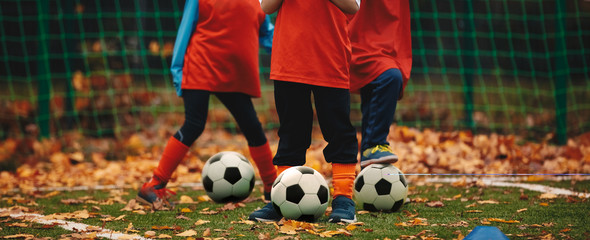 Three boys on soccer training in autumn time. Fall soccer outdoor practice session. Soccer players with ball on grass field covered with autumn leaves.