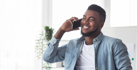 Cheerful african american guy talking on cellphone indoors