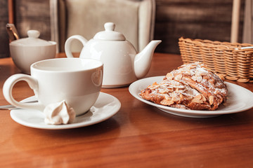 White tea cup, tea pot and fresh croissant on table in cafe, close up