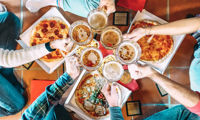 Young friends roomates eating take away pizza at home after college - Friendship concept with people students enjoying time together and having fun at shared apartment - Focus on beer pint glasses
