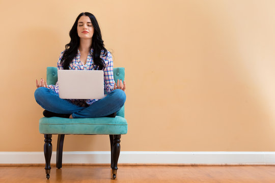 Young woman with laptop in a meditation pose pose sitting in a chair