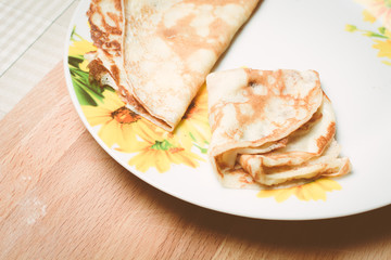 Yellow pancakes for breakfast in large plate on wooden board.