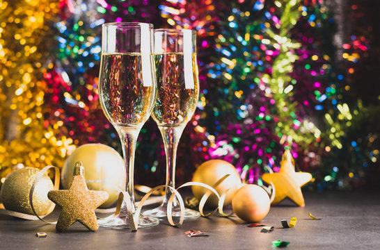 Champagne in two glasses golden Christmas toys serpentine star balls on a bright festive background. New Year concept.